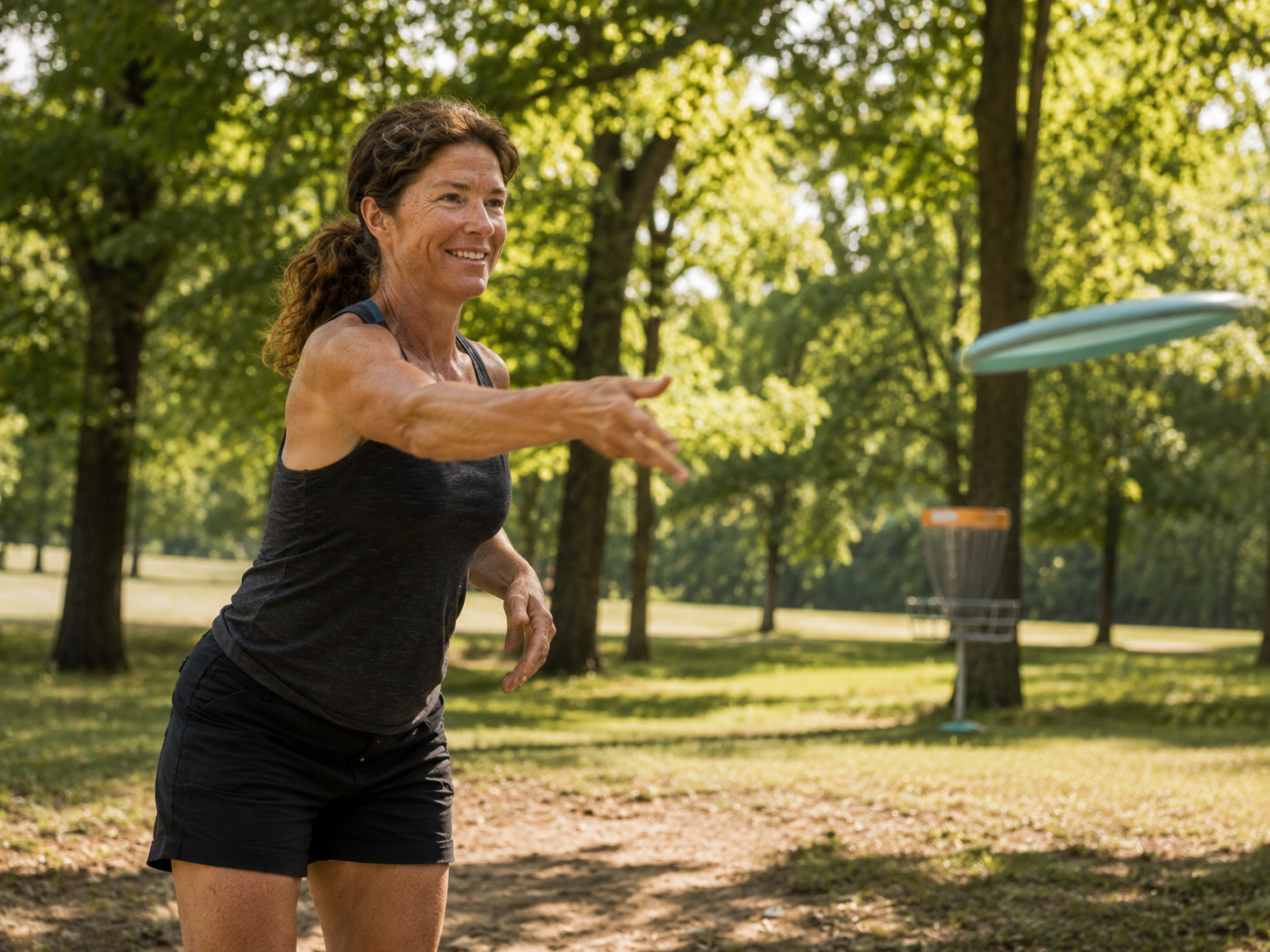 A woman mid-throw with a disc in a sunny green park, smiling